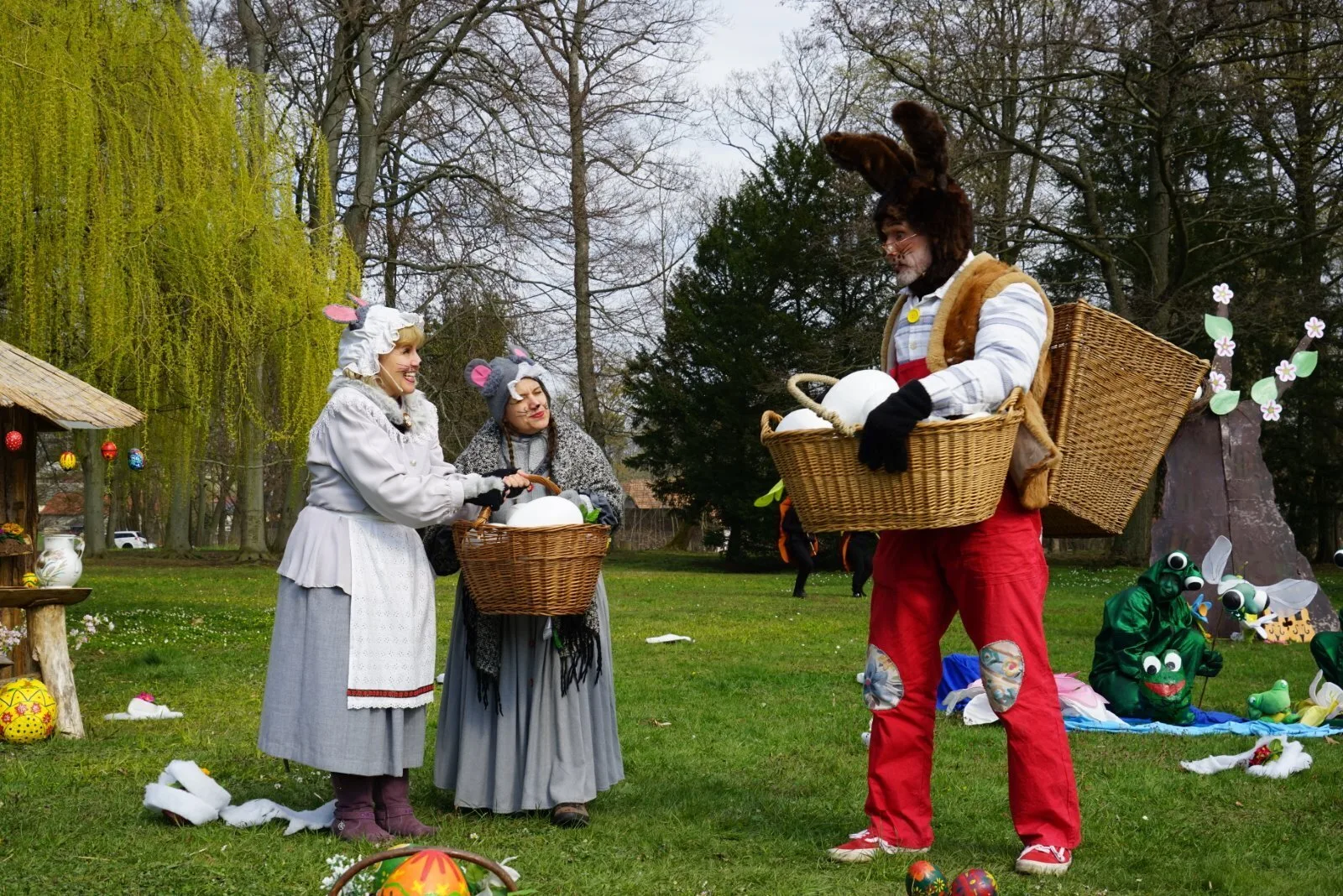 Osterhase verteilt Eier an die Mäusefrauen – Der Osterhase trägt einen großen Korb mit weißen Eiern und übergibt der Mäusefrau Eier zum Bemalen, daneben steht ihre Maustante