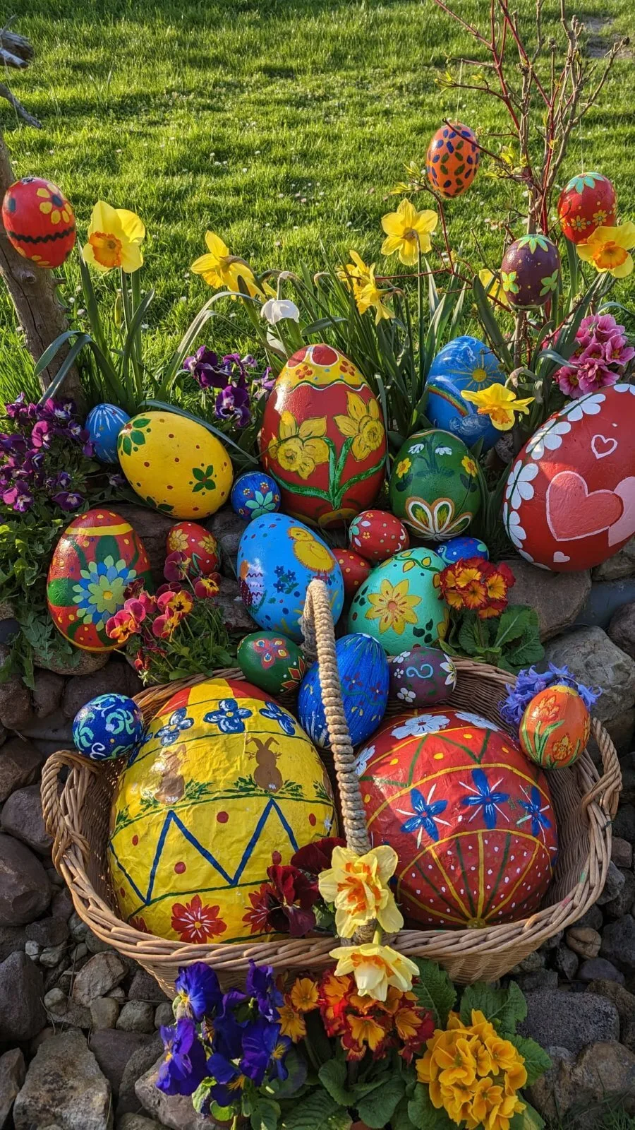 Bunte Ostereier im Frühlingsbeet – Viele handbemalte Ostereier in kräftigen Farben liegen in Körben zwischen Primeln, Narzissen und Stiefmütterchen. Das leuchtende Frühlingsbeet strahlt als festliche Dekoration im Osterdorf.