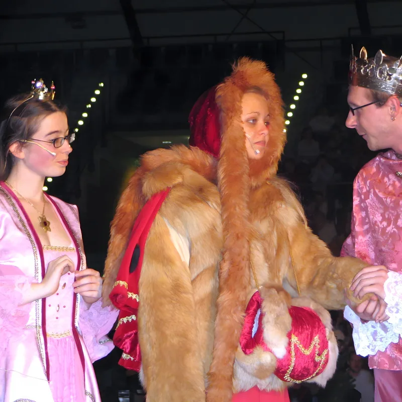 Prinzessin, König und Waldfrau beraten ? Eine Prinzessin im rosa Kleid, der König mit Krone und eine in Fell gehüllte Frau stehen eng beisammen, beraten sich vor dunkler Kulisse – königliche Sorge und Rat im Märchenreich.