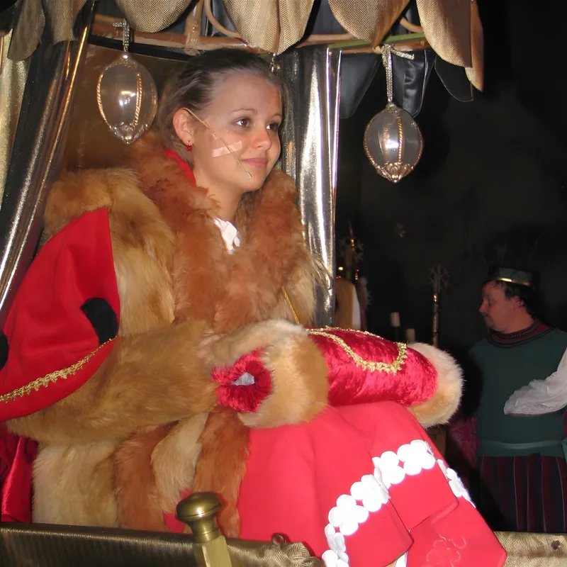 Gerda auf dem goldenen Schlitten ? Gerda in rotem Umhang und Fell sitzt nachdenklich in einem geschmückten Schlitten, glitzernde Laternen hängen über ihr – Aufbruch in die wintrige Suche.