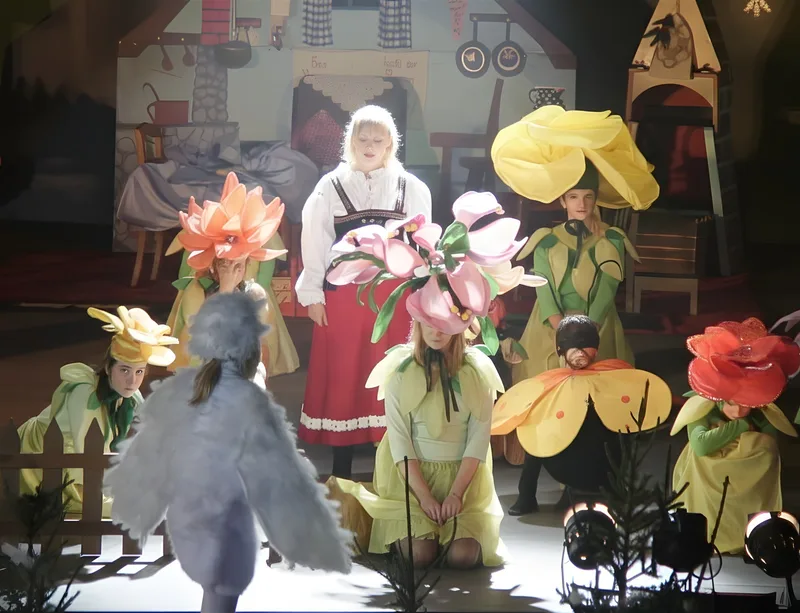 Gerda im Blumengarten ? Gerda in weiß-rotem Kleid begegnet Blumenmädchen mit riesigen Blütenhüten, ein Vogelkind schaut zu – Traumsequenz der Verführung.