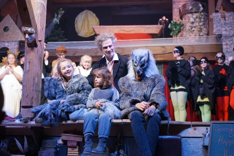 Werwölfe und Dorfbewohner nach dem Musical-Finale ? Kinder in grauen Wolfsfellen sitzen lachend neben Danius, während Werwölfe und Dorfbewohner den Schlussapplaus genießen.