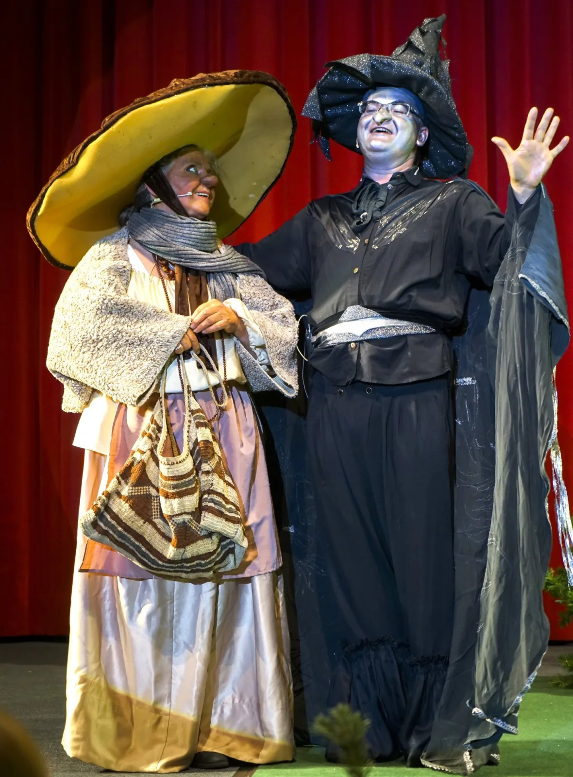 Frau Steinpilz trifft den Zauberer – Frau Steinpilz mit riesigem Hut steht lächelnd neben einem schwarzsilbern gekleideten Zauberer, beide grüßen das Publikum – freundliche Begegnung im Wald.