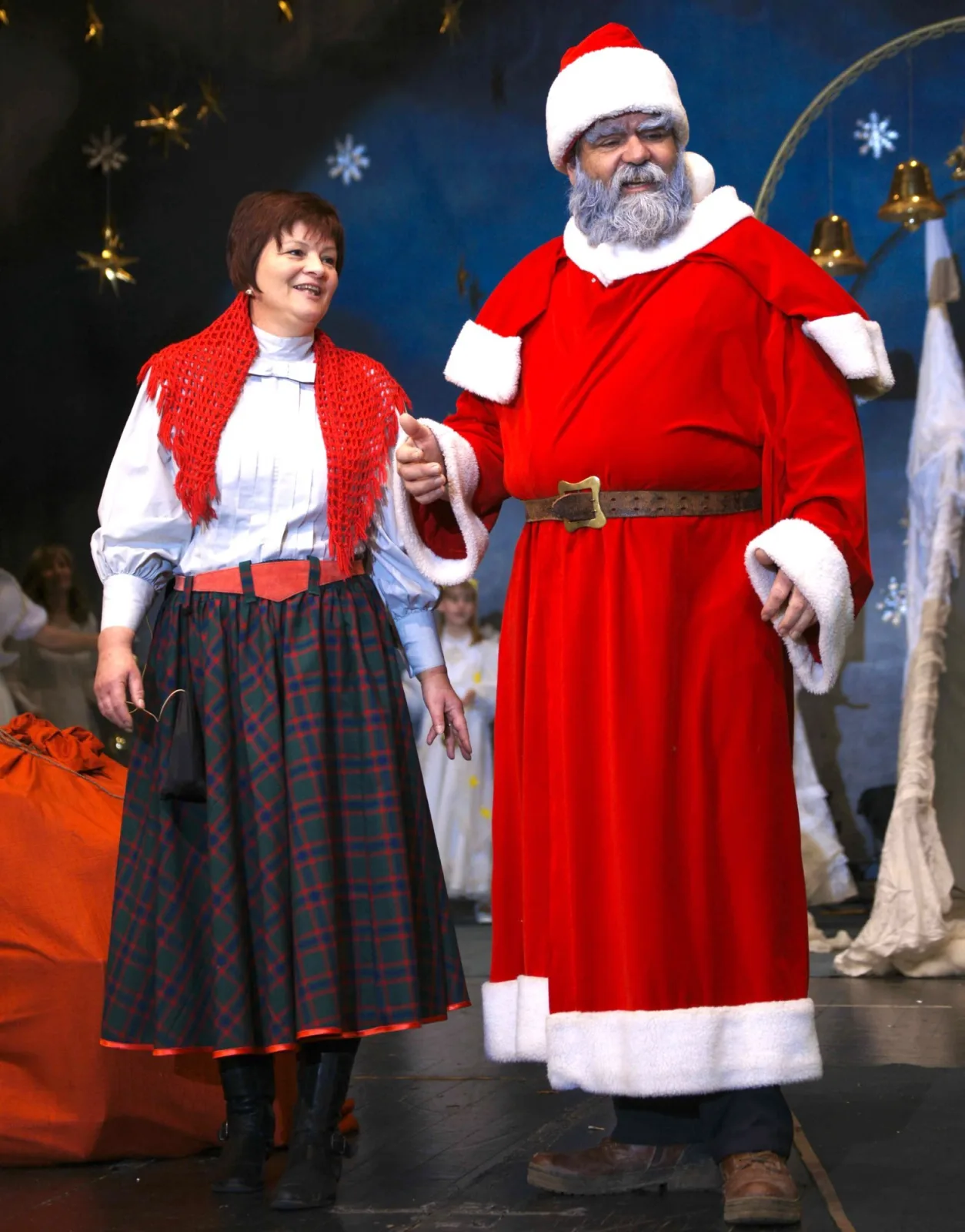 Weihnachtsmann und Weihnachtsfrau im winterlichen Himmelszelt – Der Weihnachtsmann in roter Robe steht lächelnd neben seiner Weihnachtsfrau mit rotem Schultertuch, hinter ihnen schimmern Sterne und Glockenbögen – freundliche Begrüßung im Finale.
