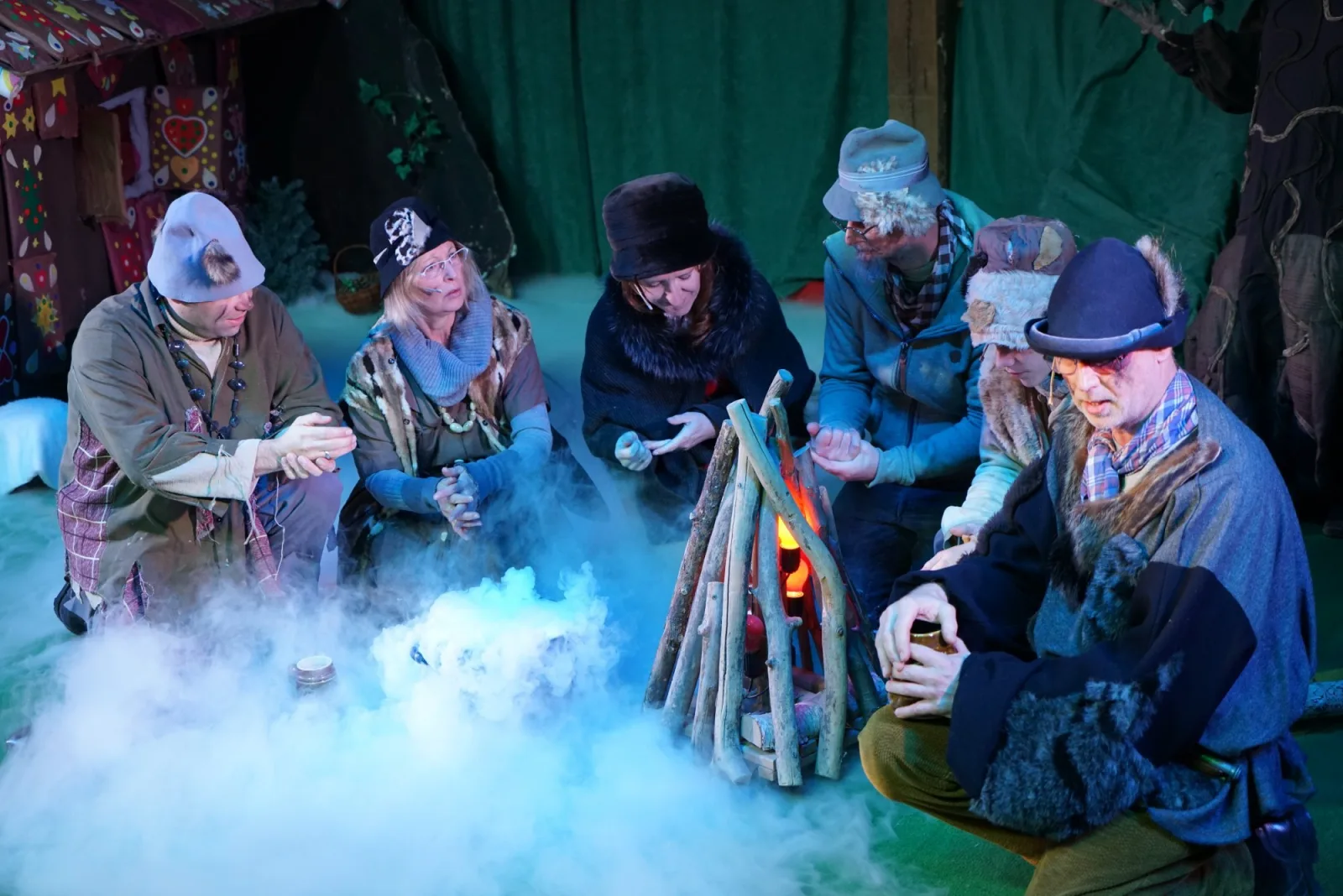 Räuber am Nebelfeuer Wald – Ein Kreis von Räubern wärmt sich am flackernden Lagerfeuer, dichter Nebel zieht über den Boden, dahinter ragen Tannen und das Knusperhäuschen – stimmungsvolle Winterpause im Märchenwald.