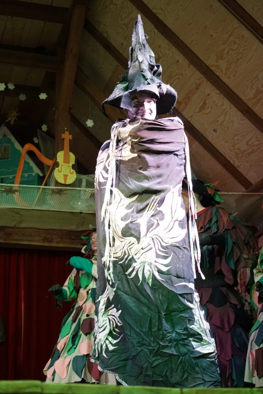 Zauberer im Märchenwald – Der schwarzsilberne Zauberer gleitet mit langem, ornamentiertem Mantel auf der Bühne dahin, der Spitzhut funkelt im Licht