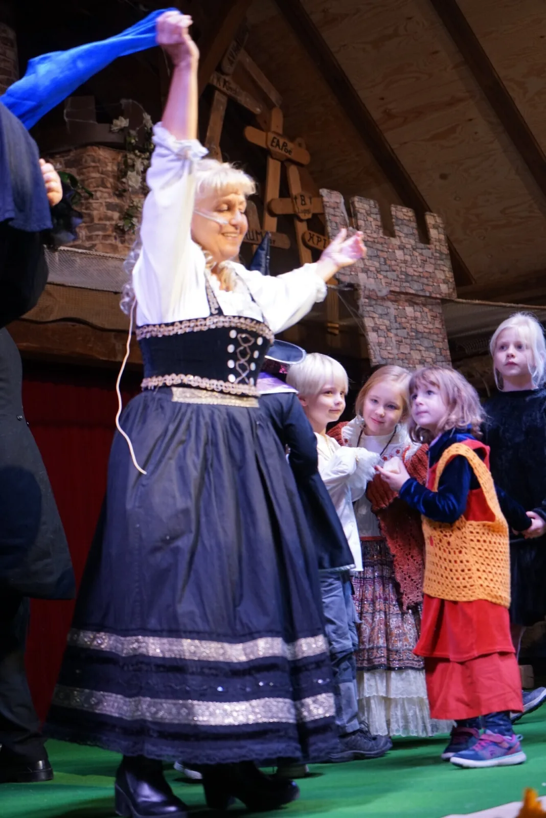 Bäckerin mit Kindern auf der Musicalbühne – Die Bäckerin hebt freudig ein Tuch, umgeben von Kindern in Kostümen, während die Szene des Dorfes lebendig wird.