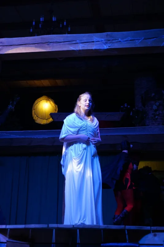 Enya im weißen Gewand singt unter Mondschein – Eine junge Frau im weißen Kleid singt ergriffen allein im Bühnenlicht, während Fledermausdarsteller im Hintergrund agieren.
